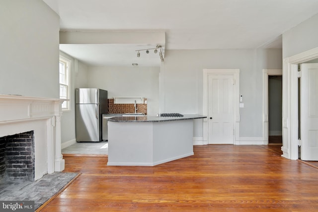 kitchen with light hardwood / wood-style flooring, stainless steel refrigerator, dark stone counters, and sink