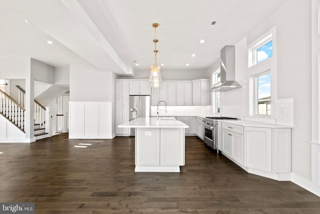 kitchen featuring high quality appliances, a kitchen island with sink, wall chimney range hood, sink, and decorative light fixtures