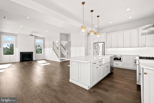 kitchen featuring white cabinetry, a kitchen island with sink, a large fireplace, and decorative light fixtures