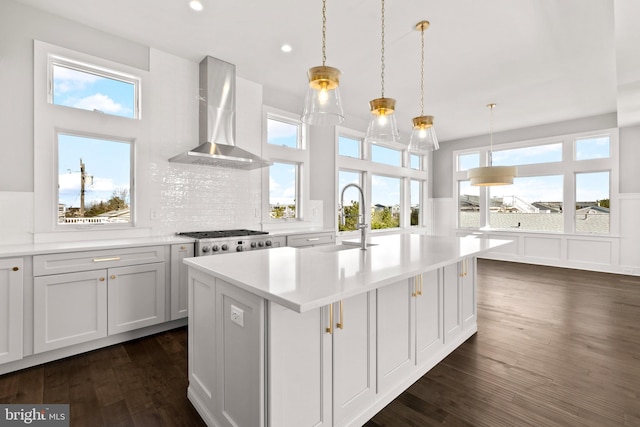 kitchen with backsplash, a kitchen island with sink, wall chimney range hood, sink, and decorative light fixtures