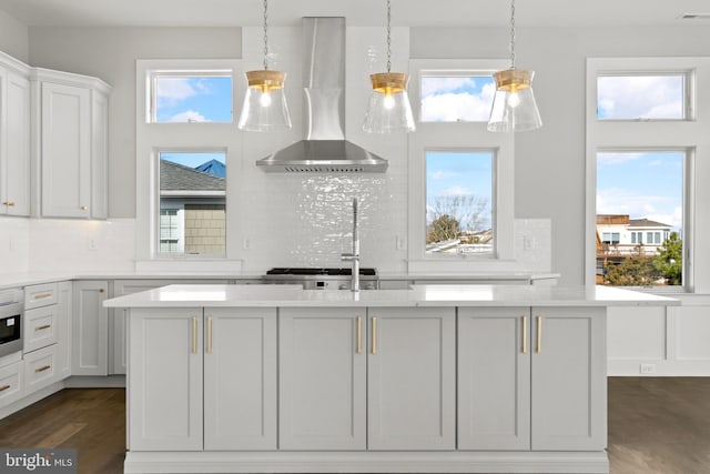 kitchen with a center island with sink, wall chimney exhaust hood, white cabinetry, and decorative backsplash