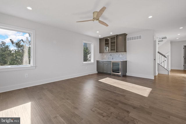 unfurnished living room with wine cooler, sink, a healthy amount of sunlight, and dark hardwood / wood-style flooring