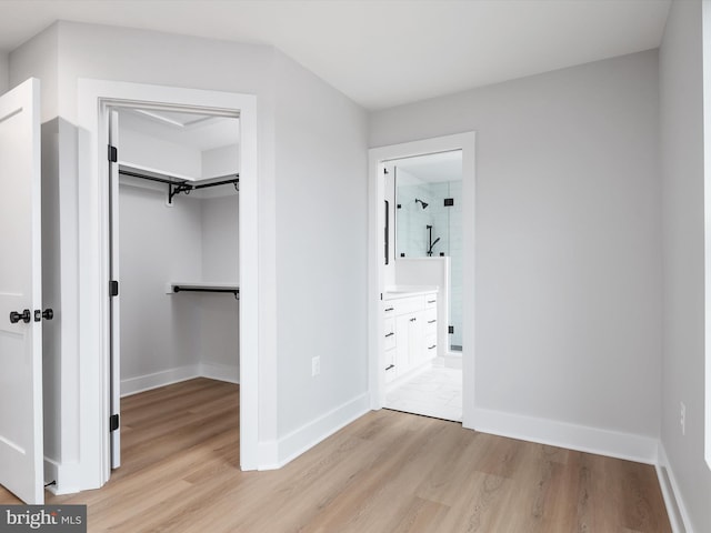 unfurnished bedroom featuring ensuite bathroom, a closet, and light hardwood / wood-style floors