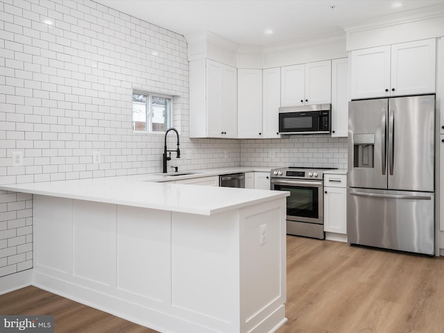 kitchen featuring light wood-type flooring, white cabinetry, kitchen peninsula, and appliances with stainless steel finishes