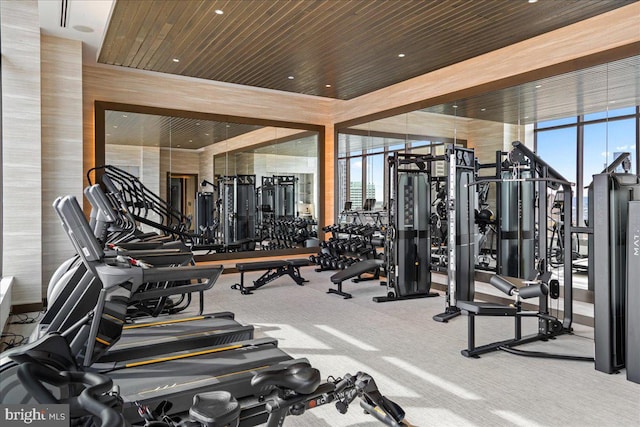 exercise room with wood ceiling, a wealth of natural light, floor to ceiling windows, and carpet flooring