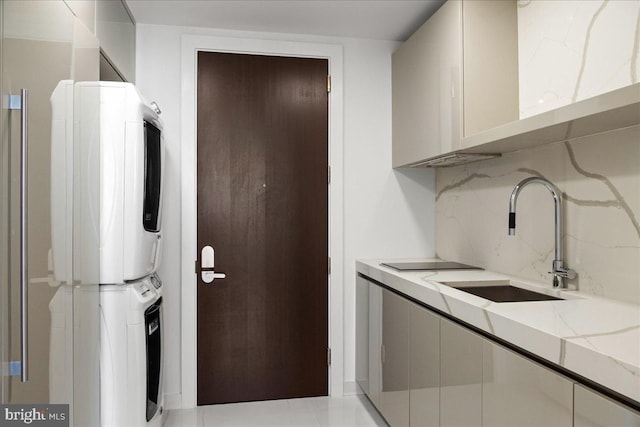 laundry area featuring sink, light tile floors, and stacked washing maching and dryer