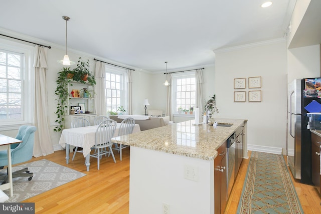 kitchen with appliances with stainless steel finishes, light stone counters, an island with sink, sink, and light hardwood / wood-style flooring