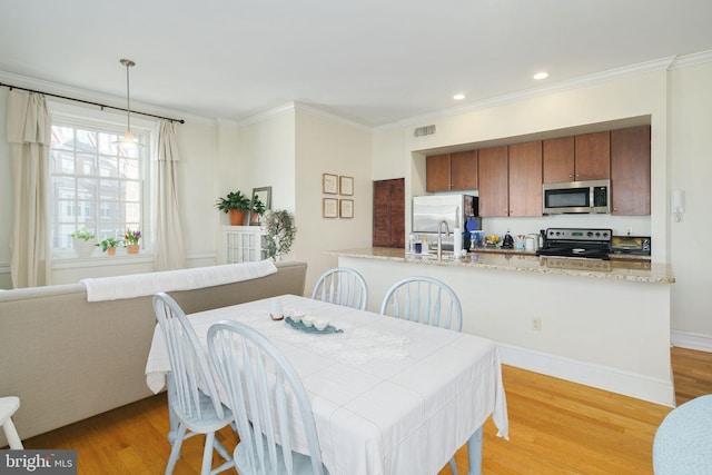 dining room with sink, ornamental molding, and light hardwood / wood-style floors