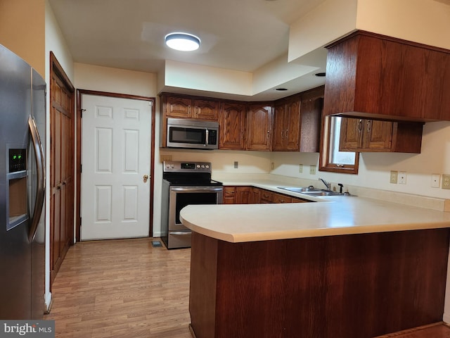 kitchen with light hardwood / wood-style floors, kitchen peninsula, sink, and appliances with stainless steel finishes