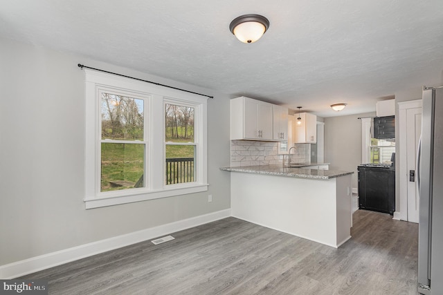 kitchen with hardwood / wood-style floors, white cabinetry, kitchen peninsula, sink, and light stone counters