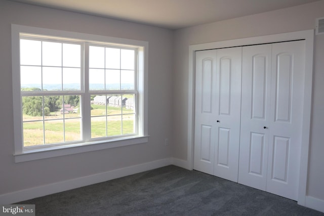 unfurnished bedroom with dark colored carpet, a closet, and multiple windows