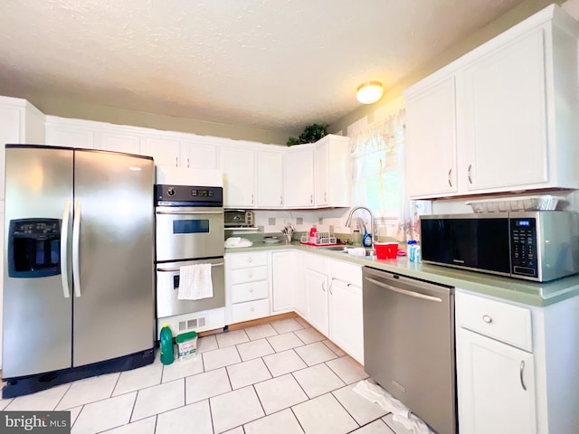 kitchen with light tile flooring, stainless steel appliances, white cabinetry, and sink