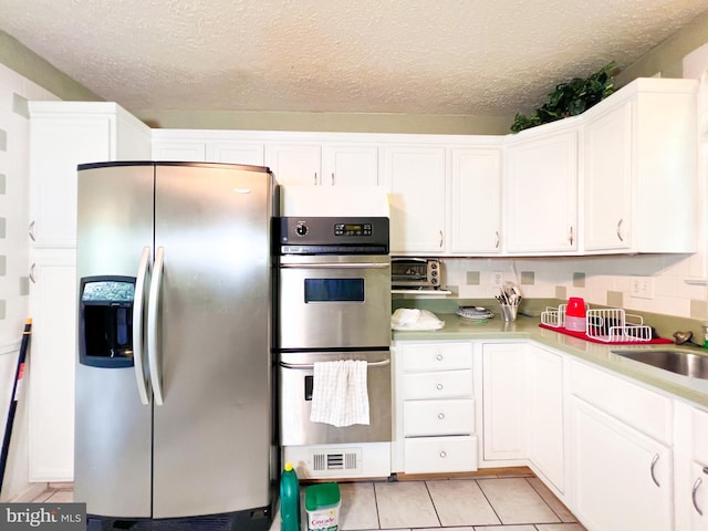 kitchen with stainless steel appliances, light tile floors, white cabinets, backsplash, and sink