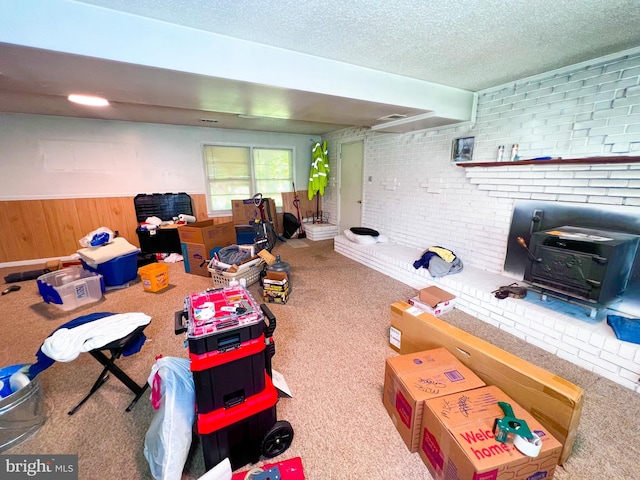 recreation room with carpet flooring, a fireplace, brick wall, a textured ceiling, and a wood stove