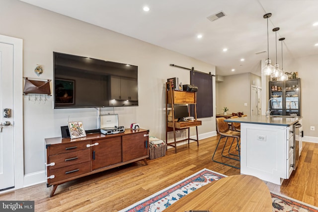 kitchen featuring a barn door, a breakfast bar area, light hardwood / wood-style flooring, pendant lighting, and sink