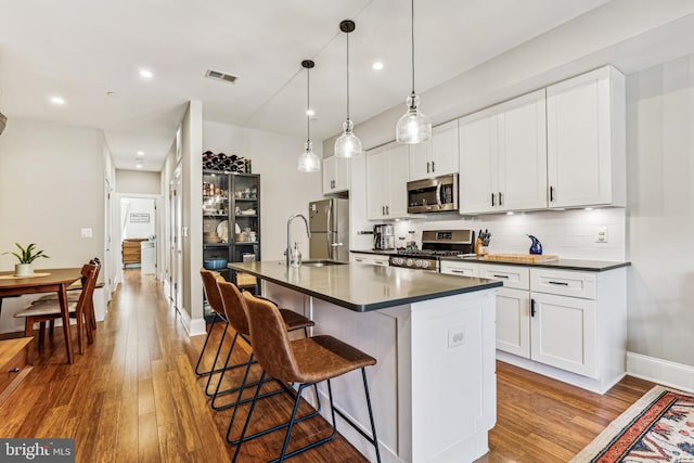 kitchen with white cabinetry, appliances with stainless steel finishes, sink, an island with sink, and light wood-type flooring