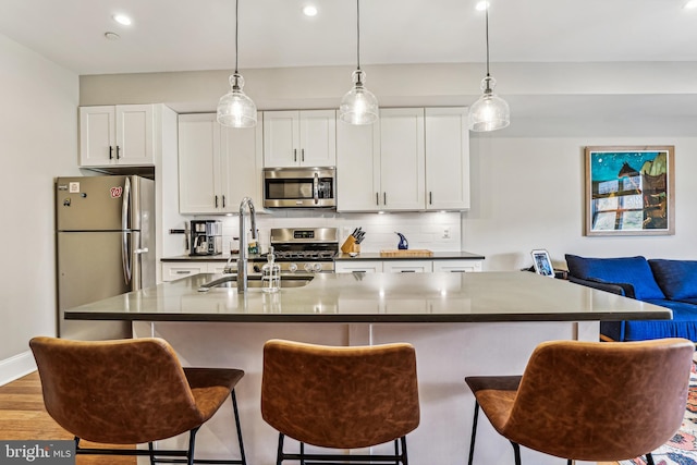 kitchen featuring appliances with stainless steel finishes, white cabinetry, a center island with sink, light hardwood / wood-style flooring, and backsplash