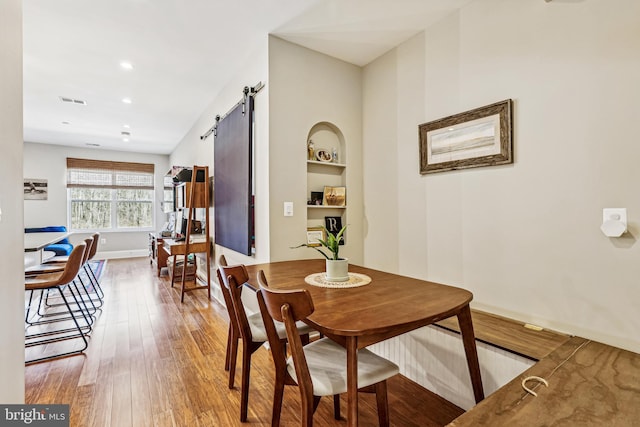 dining space featuring a barn door, built in shelves, and hardwood / wood-style flooring