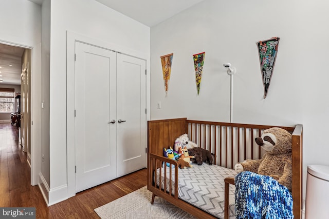 bedroom with a crib, a closet, and dark hardwood / wood-style flooring