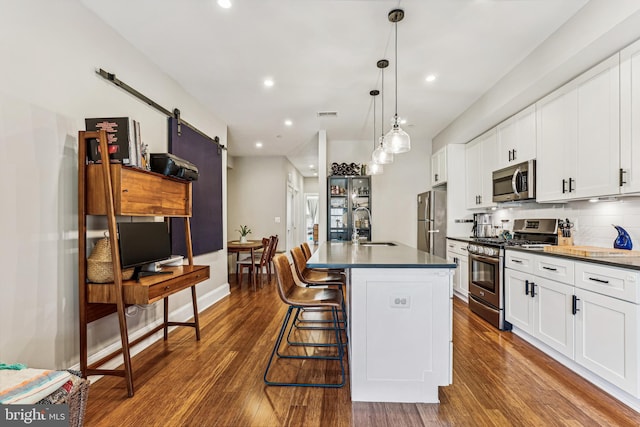 kitchen with a barn door, stainless steel appliances, pendant lighting, and dark hardwood / wood-style floors