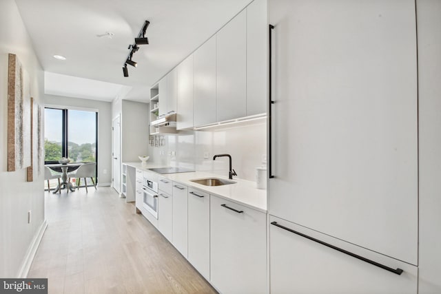 kitchen with white cabinetry, rail lighting, sink, and light wood-type flooring