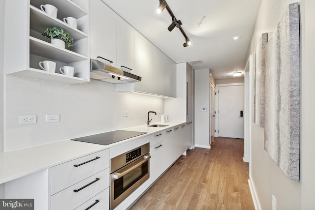 kitchen with light hardwood / wood-style floors, white cabinets, black electric stovetop, track lighting, and oven