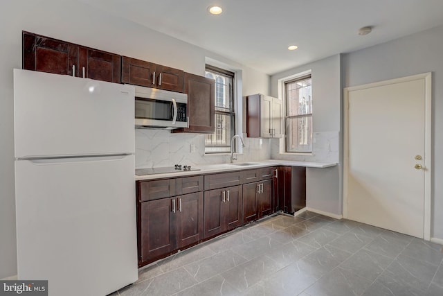 kitchen featuring white fridge, black electric stovetop, backsplash, sink, and light tile flooring