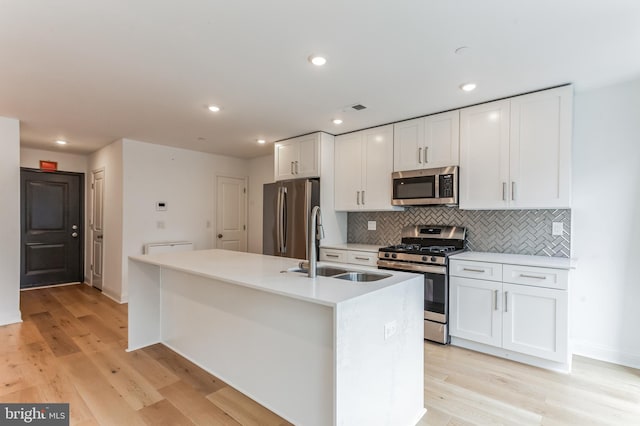 kitchen with white cabinetry, stainless steel appliances, light hardwood / wood-style flooring, a kitchen island with sink, and backsplash