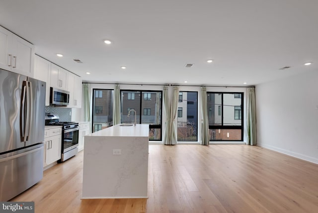 kitchen featuring tasteful backsplash, stainless steel appliances, light hardwood / wood-style flooring, a center island with sink, and white cabinets