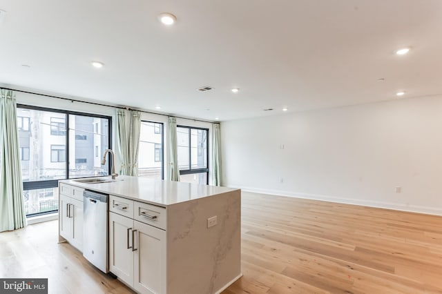 kitchen with sink, stainless steel dishwasher, a center island with sink, light hardwood / wood-style floors, and white cabinetry