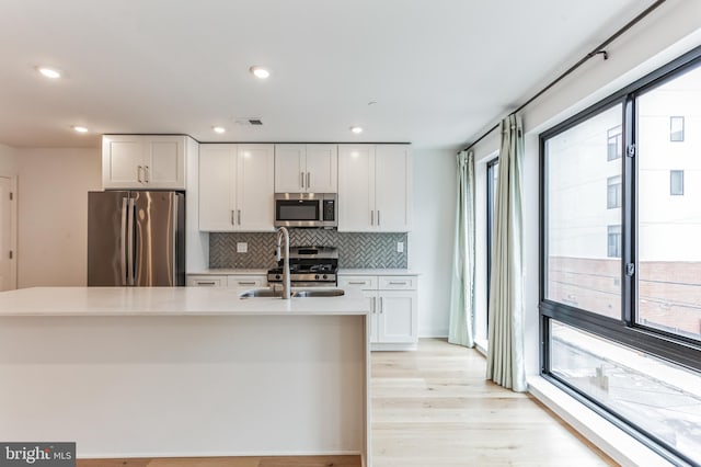 kitchen with sink, appliances with stainless steel finishes, light hardwood / wood-style flooring, backsplash, and white cabinetry