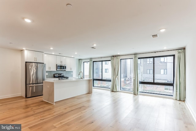 kitchen with tasteful backsplash, white cabinets, stainless steel appliances, light hardwood / wood-style flooring, and a kitchen island with sink