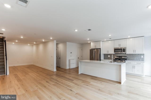 kitchen with white cabinets, an island with sink, stainless steel appliances, and light wood-type flooring