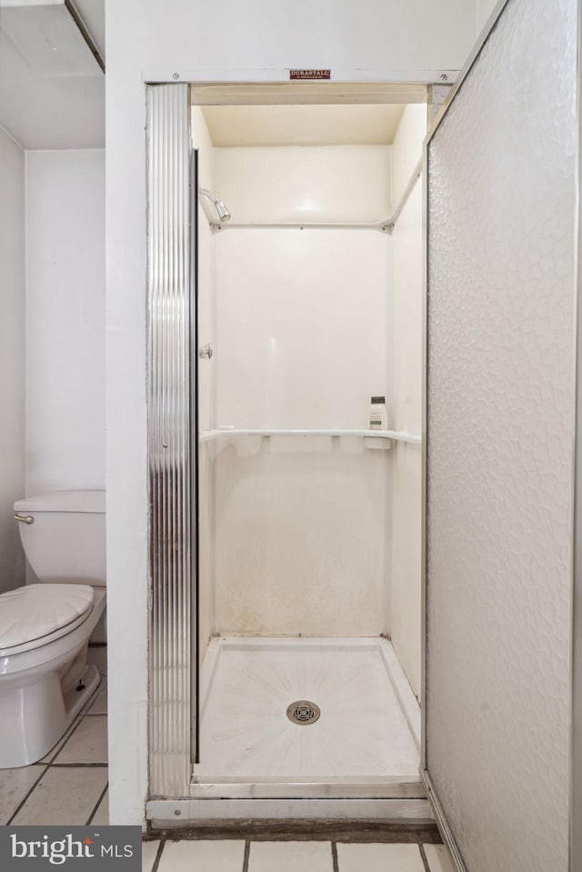 bathroom with a shower, toilet, and tile flooring