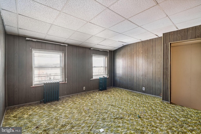 spare room featuring carpet floors, wood walls, and radiator