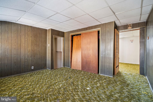 unfurnished bedroom featuring a closet, wooden walls, a paneled ceiling, and carpet floors