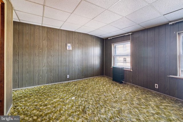 spare room featuring carpet floors, wooden walls, and radiator heating unit