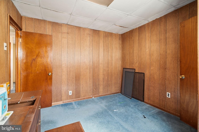 carpeted spare room featuring wooden walls and a paneled ceiling