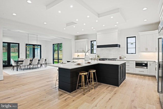 kitchen featuring a large island, a breakfast bar, white cabinets, and premium range hood