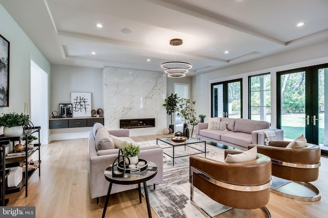 living room featuring a tray ceiling, a fireplace, french doors, and light wood-type flooring