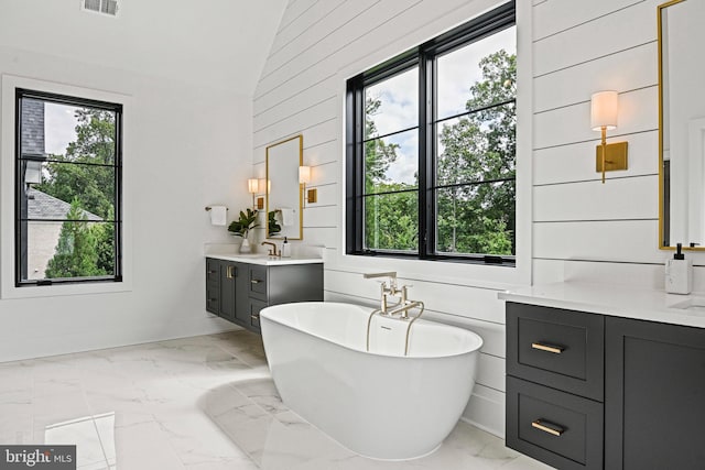 bathroom featuring vanity, a tub, plenty of natural light, and lofted ceiling