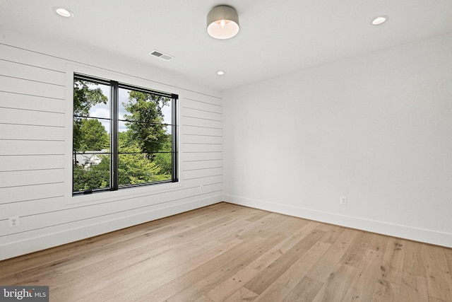 unfurnished room with light hardwood / wood-style flooring, wooden walls, and a healthy amount of sunlight