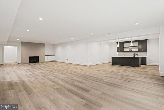 unfurnished living room with indoor bar, a large fireplace, and light hardwood / wood-style flooring