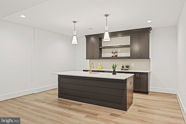 bar with tasteful backsplash, sink, hanging light fixtures, dark brown cabinetry, and light hardwood / wood-style flooring