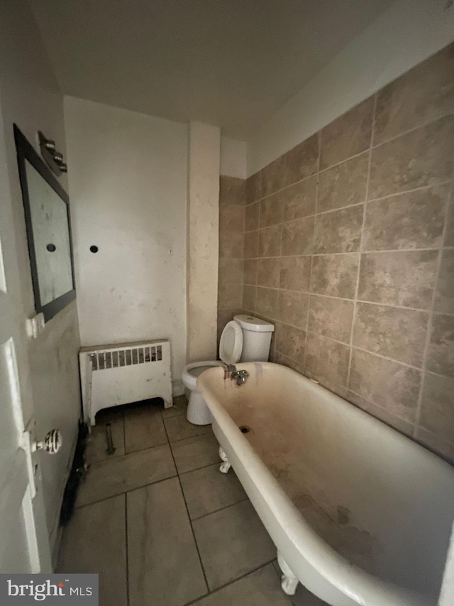 bathroom featuring radiator heating unit, toilet, tile floors, and tile walls