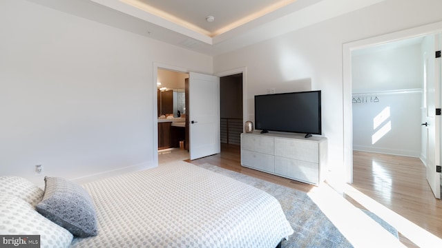 bedroom with light hardwood / wood-style flooring, a tray ceiling, and connected bathroom