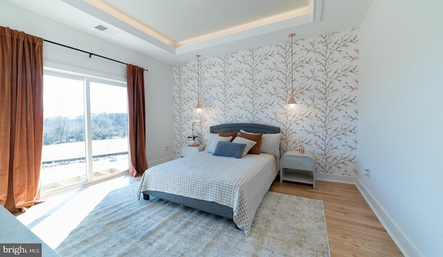 bedroom featuring light hardwood / wood-style flooring, access to exterior, and a tray ceiling