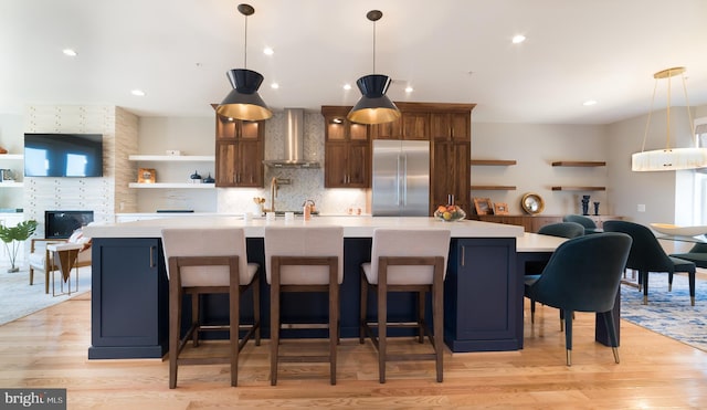 kitchen featuring built in fridge, a breakfast bar, light hardwood / wood-style floors, and wall chimney exhaust hood