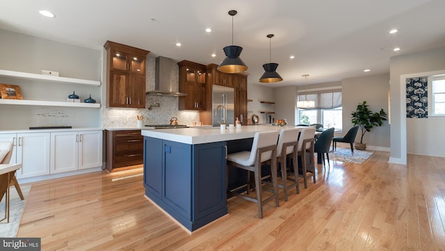 kitchen with wall chimney exhaust hood, light hardwood / wood-style flooring, a kitchen bar, a center island with sink, and tasteful backsplash