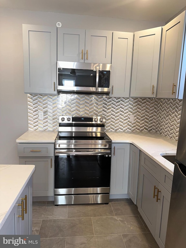 kitchen with backsplash, stainless steel appliances, gray cabinets, and dark tile flooring